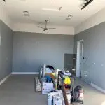 Interior room during a professional house painting project, showing freshly painted gray walls, high ceilings, and prep materials on site