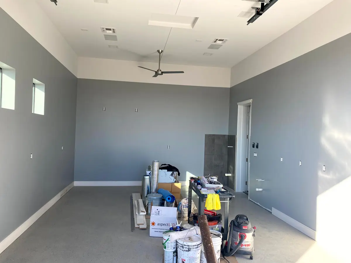 Interior room during a professional house painting project, showing freshly painted gray walls, high ceilings, and prep materials on site