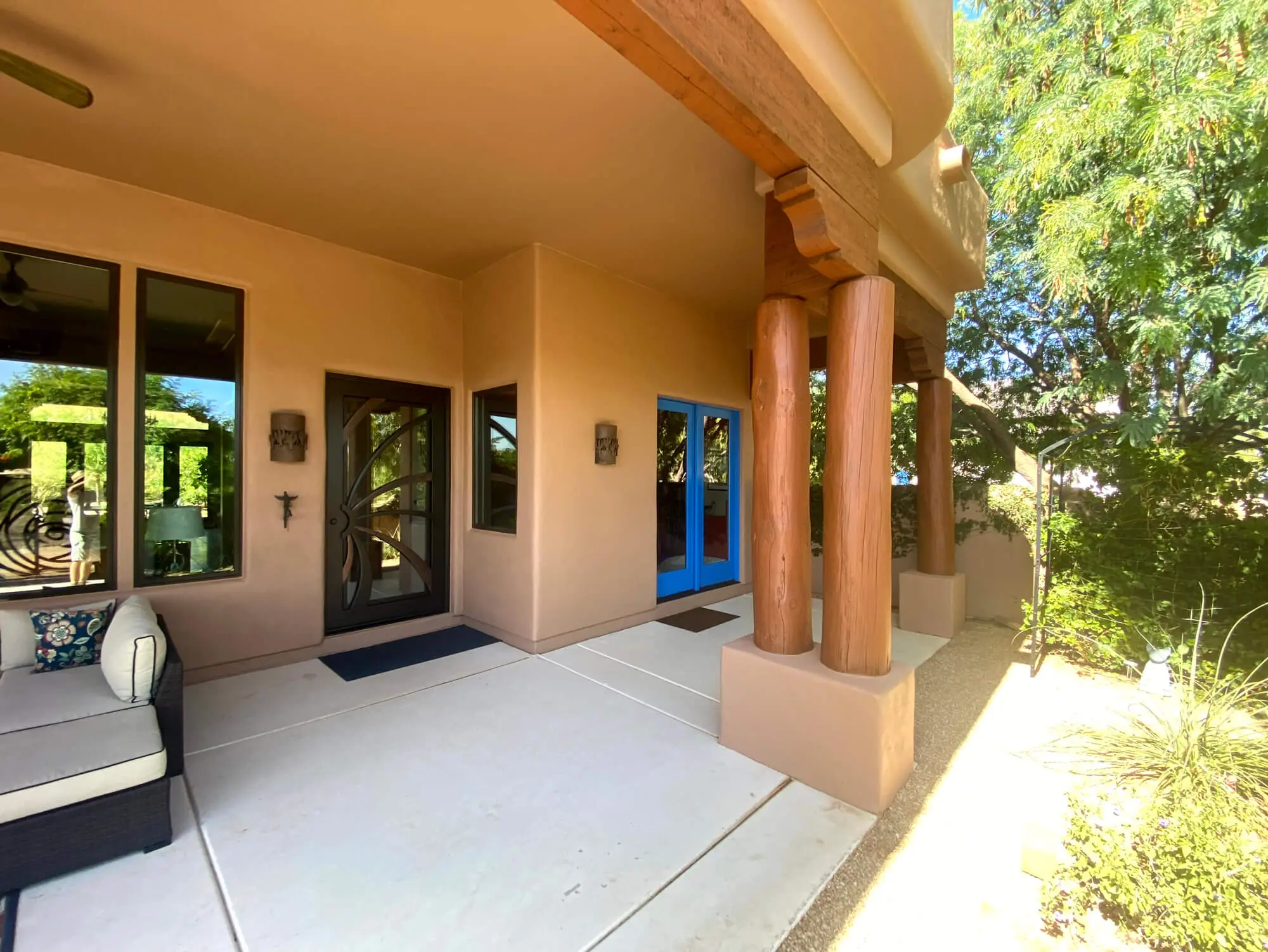 Modern Southwestern patio featuring tan stucco walls, rustic wood pillars, and a vibrant blue accent door by Butchers Custom Painting.