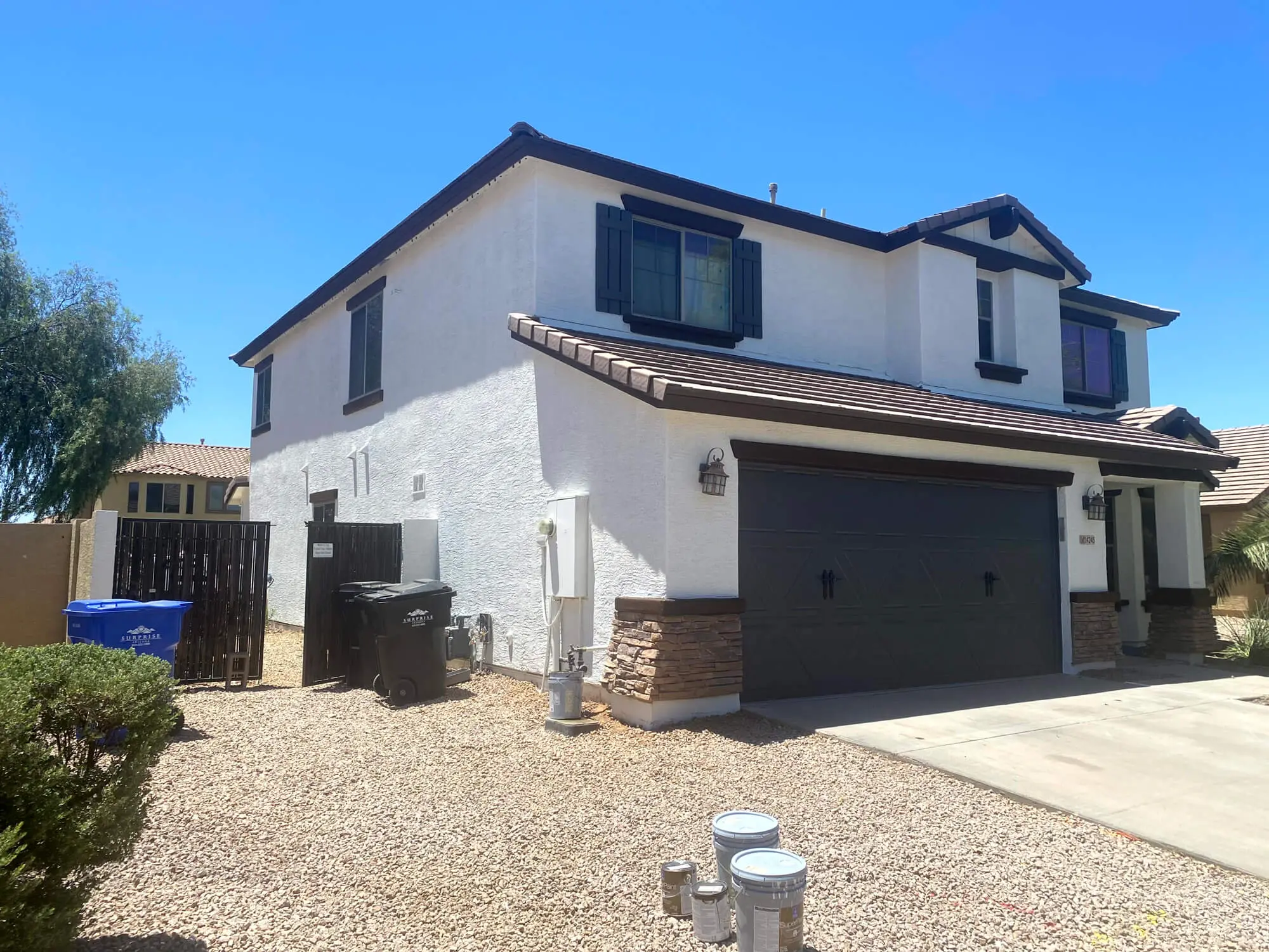 Modern two-story residential home with a crisp white stucco finish, dark brown trim, and decorative stone pillars, professionally painted by Butchers Custom Painting.
