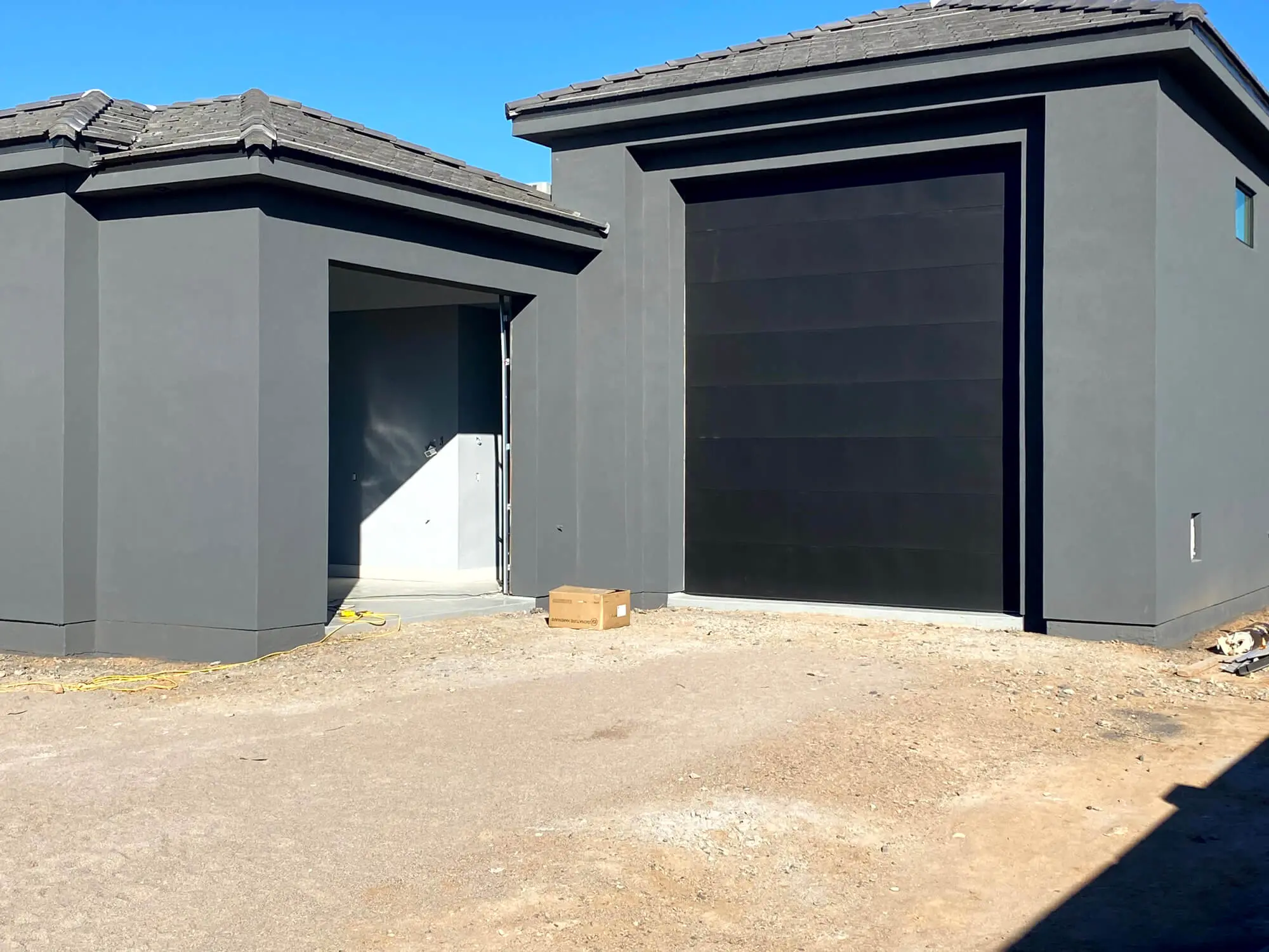 Modern residential exterior featuring a fresh charcoal grey stucco finish and matte black garage door by Butchers Custom Painting.