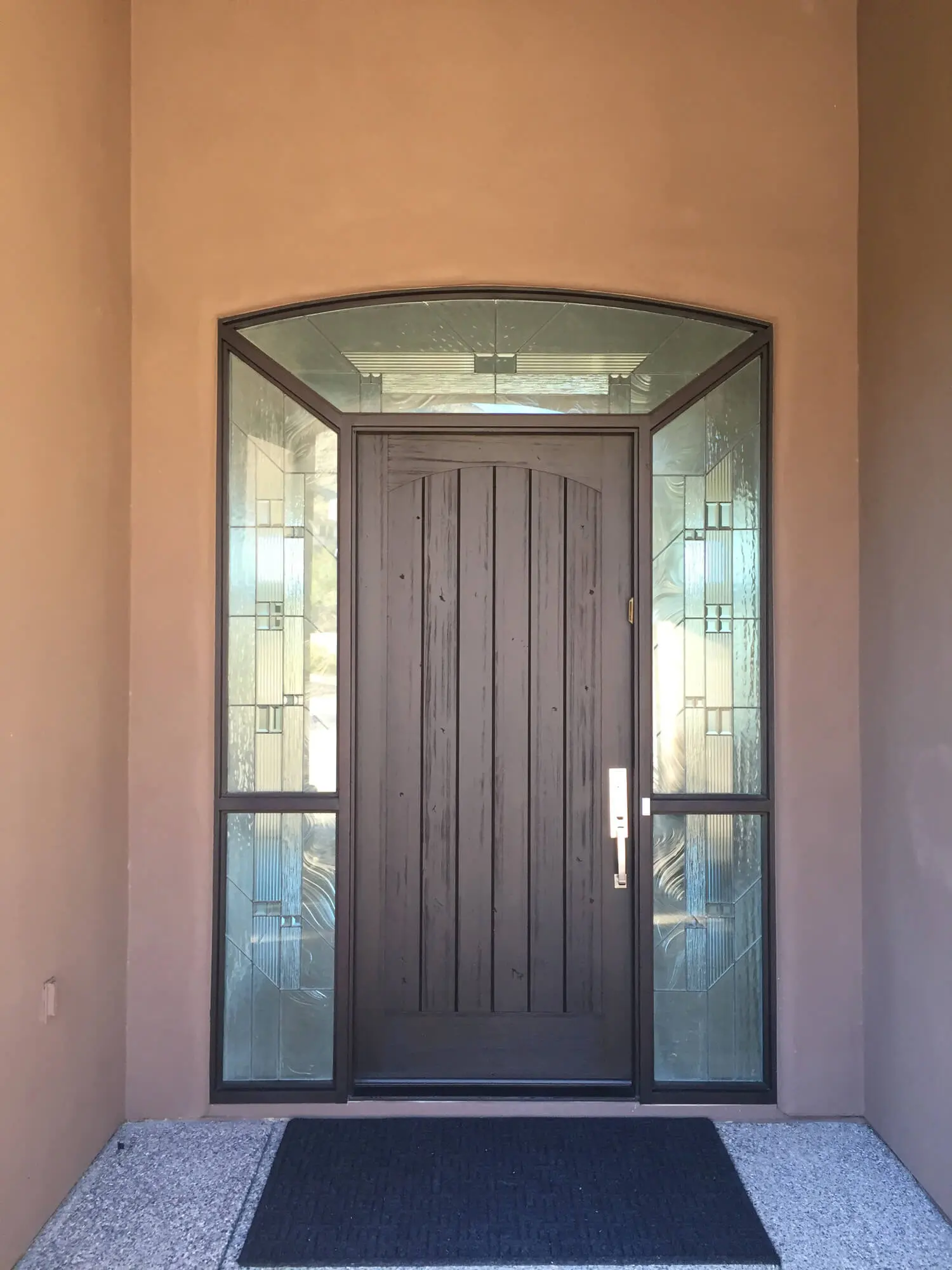 A dark wood front door by Butchers Custom Painting with decorative glass sidelights and a curved transom.