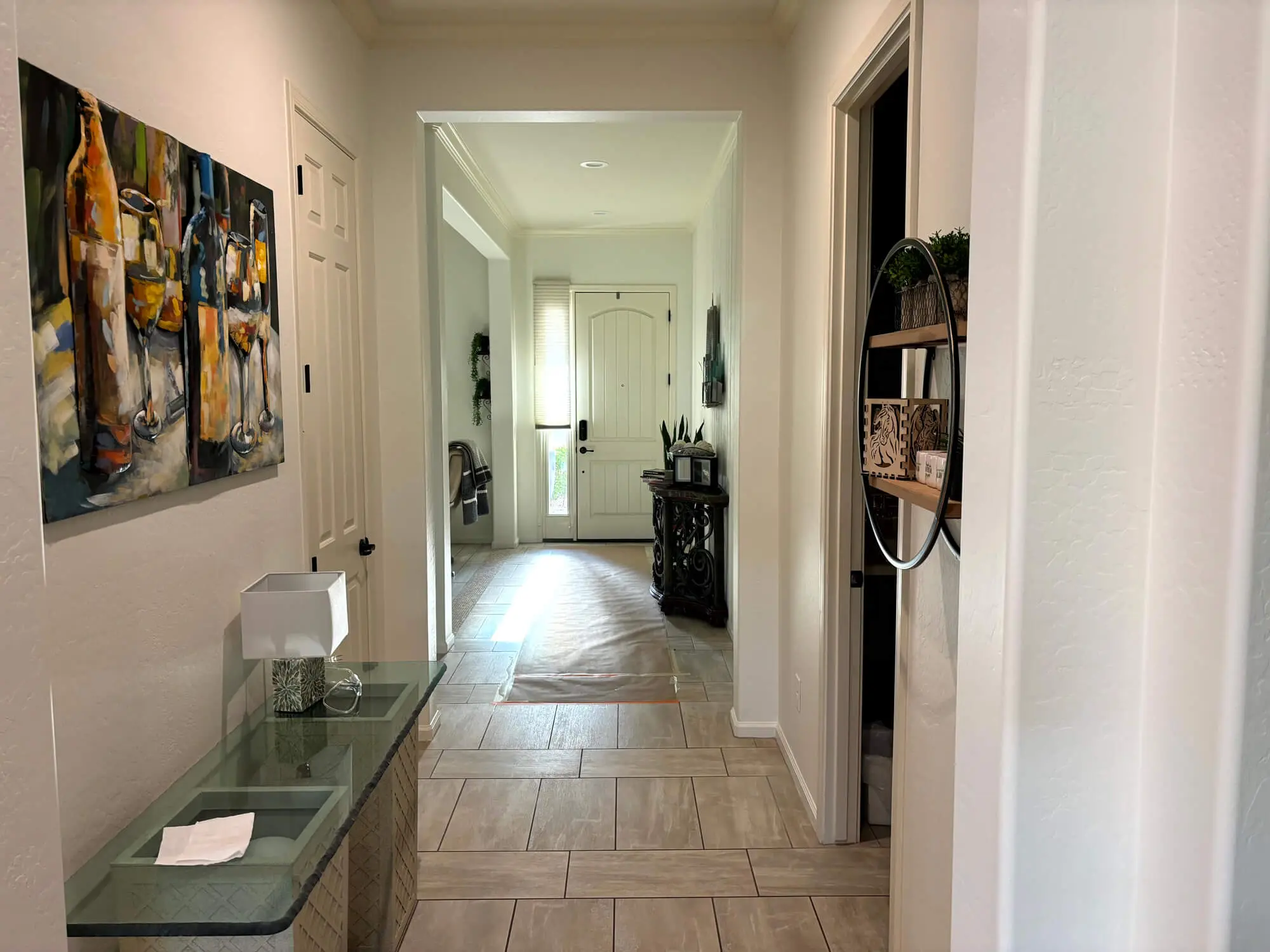 A brightly lit home hallway featuring tile flooring, artwork, and a view of the front door, professionally finished by Butchers Custom Painting.