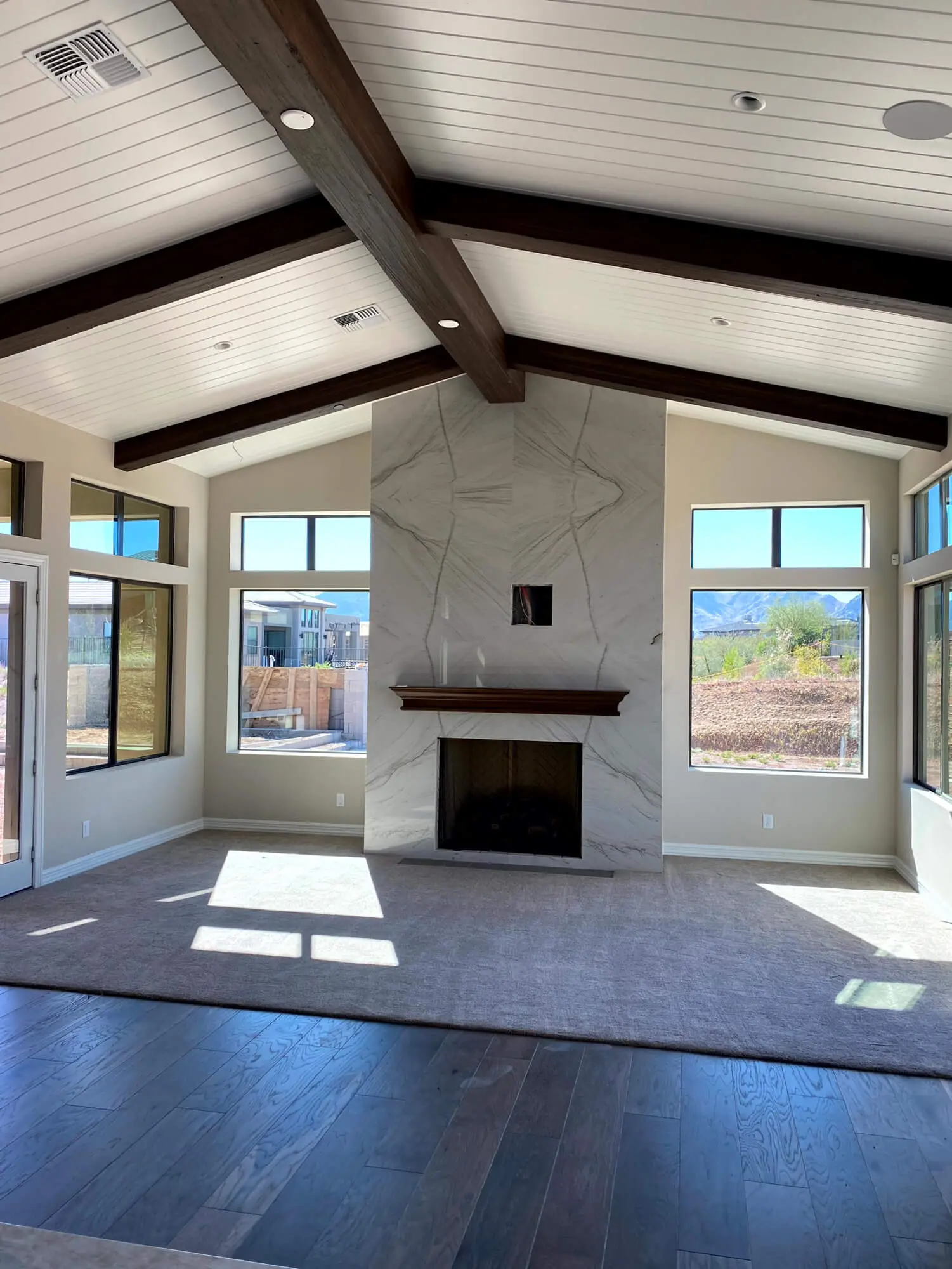 A modern living room featuring a vaulted ceiling with dark wood beams and a marble fireplace, professionally finished by Butchers Custom Painting.