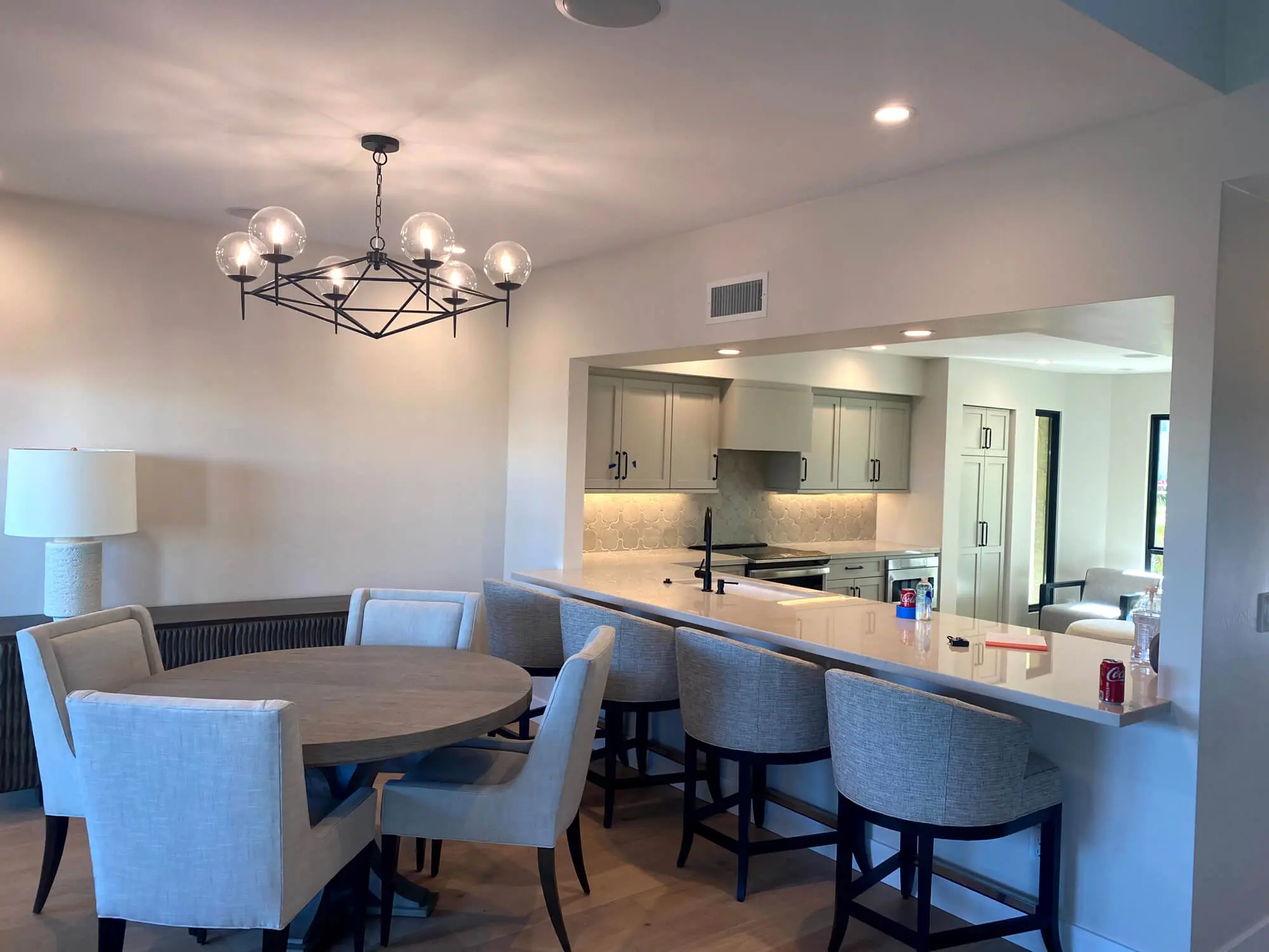 Modern dining area and kitchen featuring professional interior finishes by Butchers Custom Painting, a geometric chandelier, and elegant gray cabinetry.