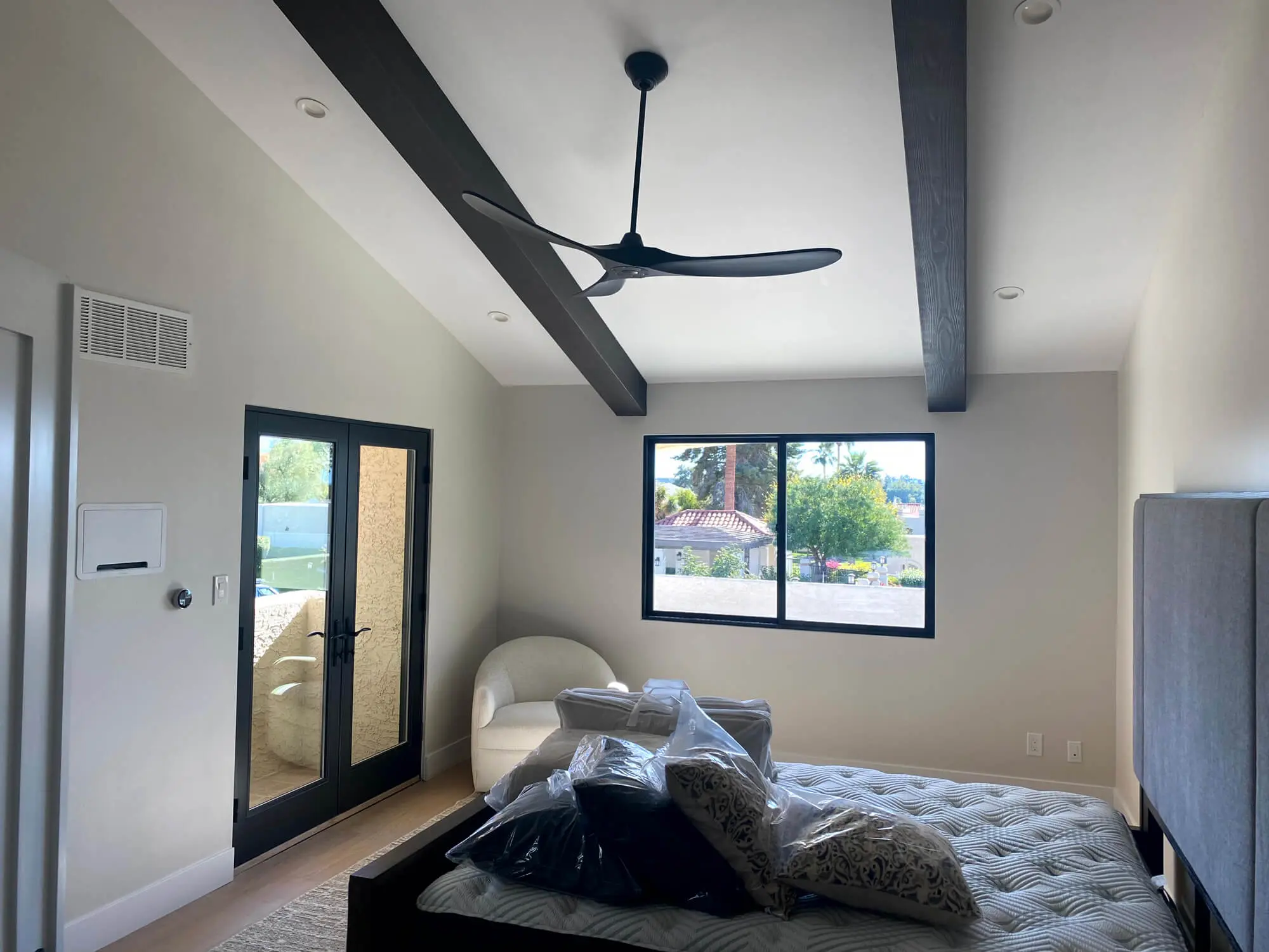Modern bedroom featuring vaulted ceilings with dark wood beams painted by Butchers Custom Painting, alongside black window frames and French doors.