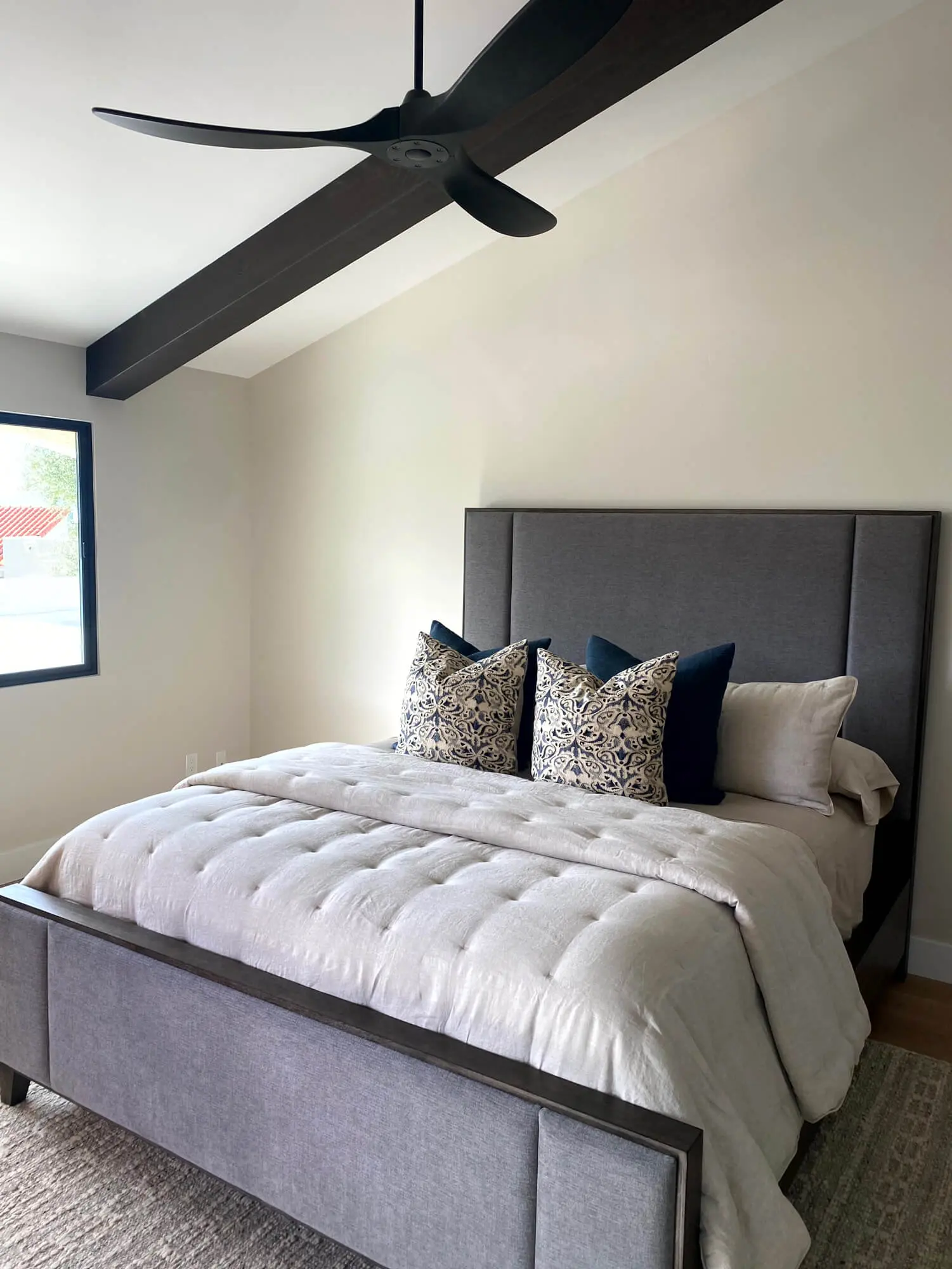 Modern master bedroom featuring a dark wood vaulted ceiling beam and neutral walls, expertly finished by Butchers Custom Painting.