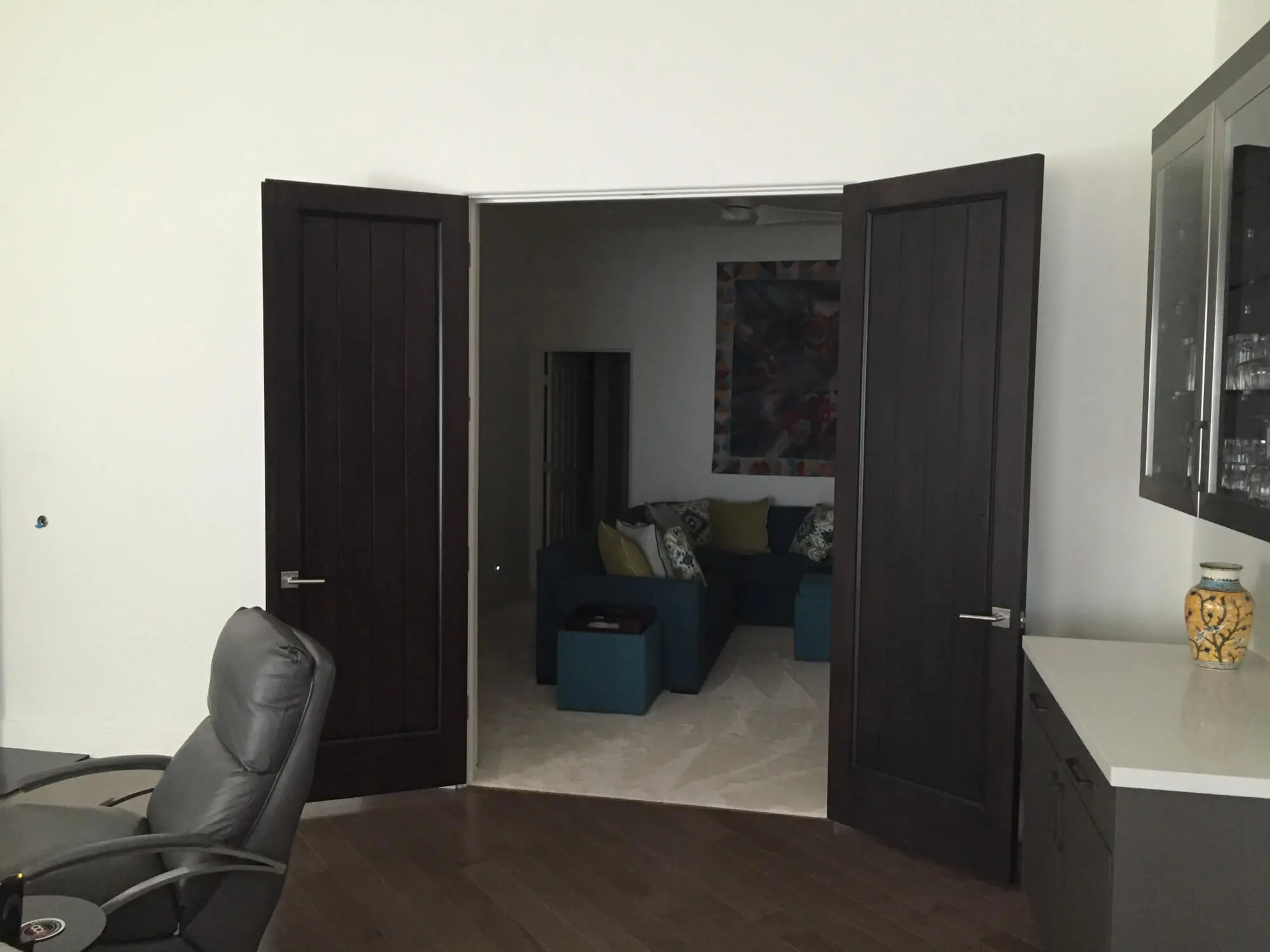 Modern dark wood double doors open to a living room with blue seating and a colorful wall mural, featuring professional interior finishes by Butchers Custom Painting.