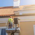 A professional painter on a lift working on a stucco home exterior in Peoria, Arizona backed by a workmanship warranty.