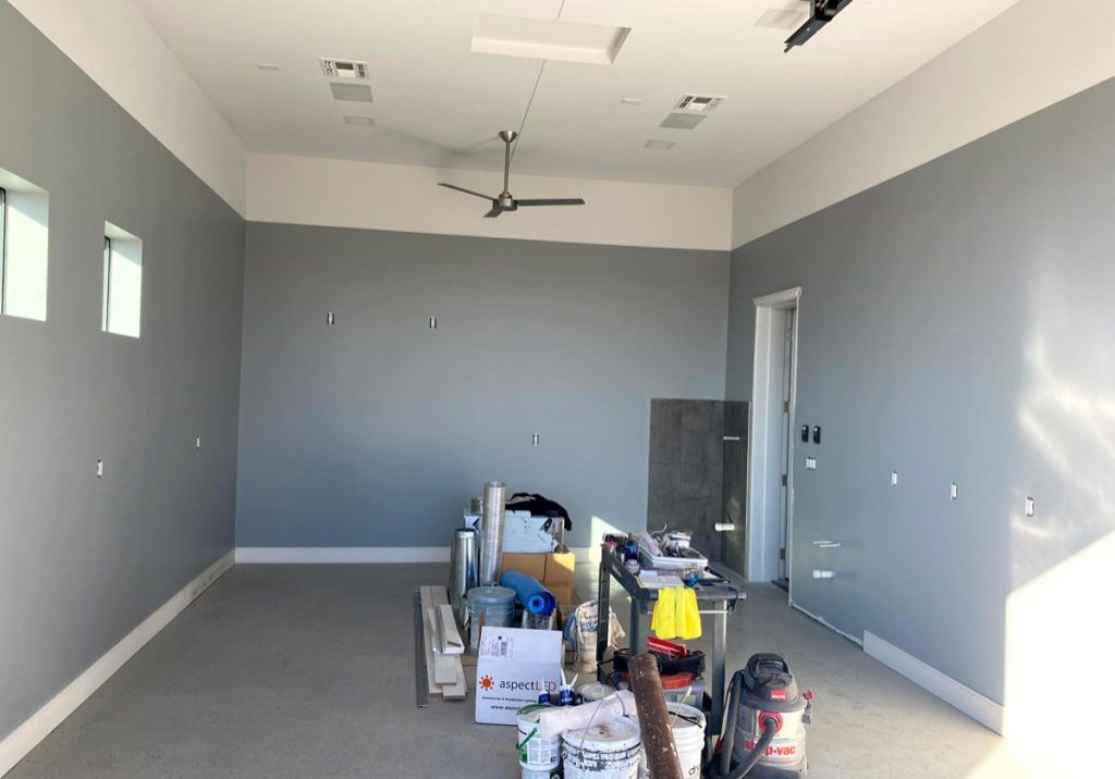 Interior room during a professional house painting project, showing freshly painted gray walls, high ceilings, and prep materials on site